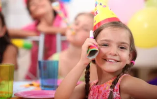 little girl at her birthday wearing a yellow party hat at indoor playground
