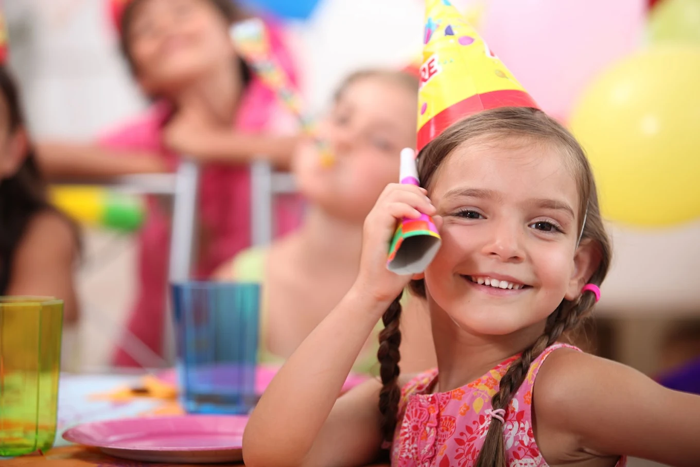 little girl at her birthday wearing a yellow party hat at indoor playground